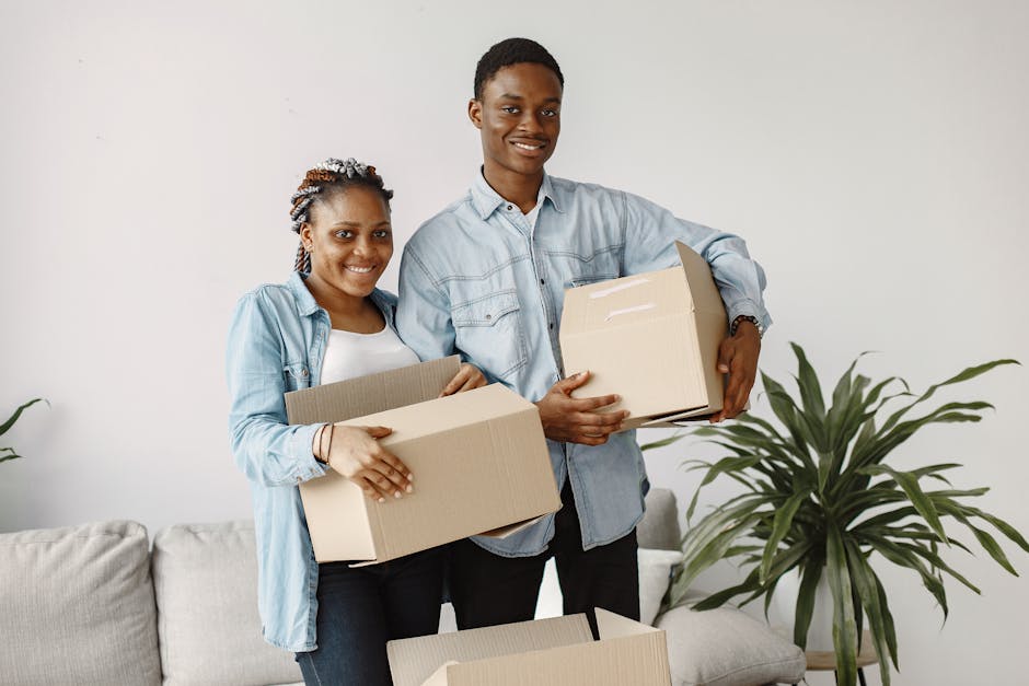 Young couple smiling while moving into a new home, holding cardboard boxes indoors.